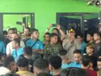 polsek Seorang perwira polisi berseragam lengkap berbicara melalui pengeras suara di tengah kerumunan ratusan kuli bongkar muat Pasar Induk Tanah Tinggi Tangerang saat aksi unjuk rasa malam hari. Beberapa pekerja terlihat mengenakan kaos biru.