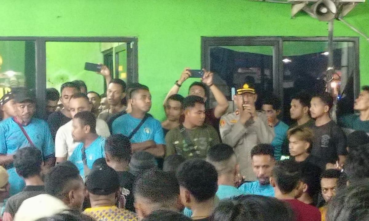 Seorang perwira polisi berseragam lengkap berbicara melalui pengeras suara di tengah kerumunan ratusan kuli bongkar muat Pasar Induk Tanah Tinggi Tangerang saat aksi unjuk rasa malam hari. Beberapa pekerja terlihat mengenakan kaos biru.
