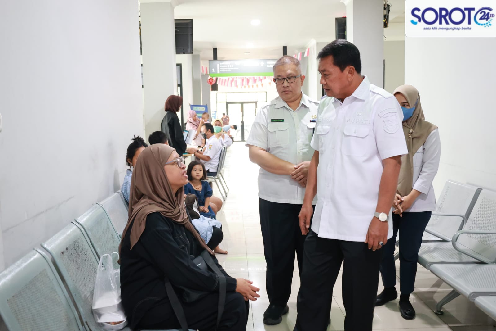 Bupati Maesyal berdiri berbincang dengan ibu-ibu pasien di kursi tunggu Puskesmas