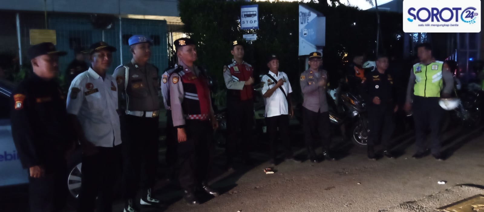 Beberapa petugas berseragam berdiri di area parkir malam hari dengan motor dan petugas Dishub memakai rompi oranye