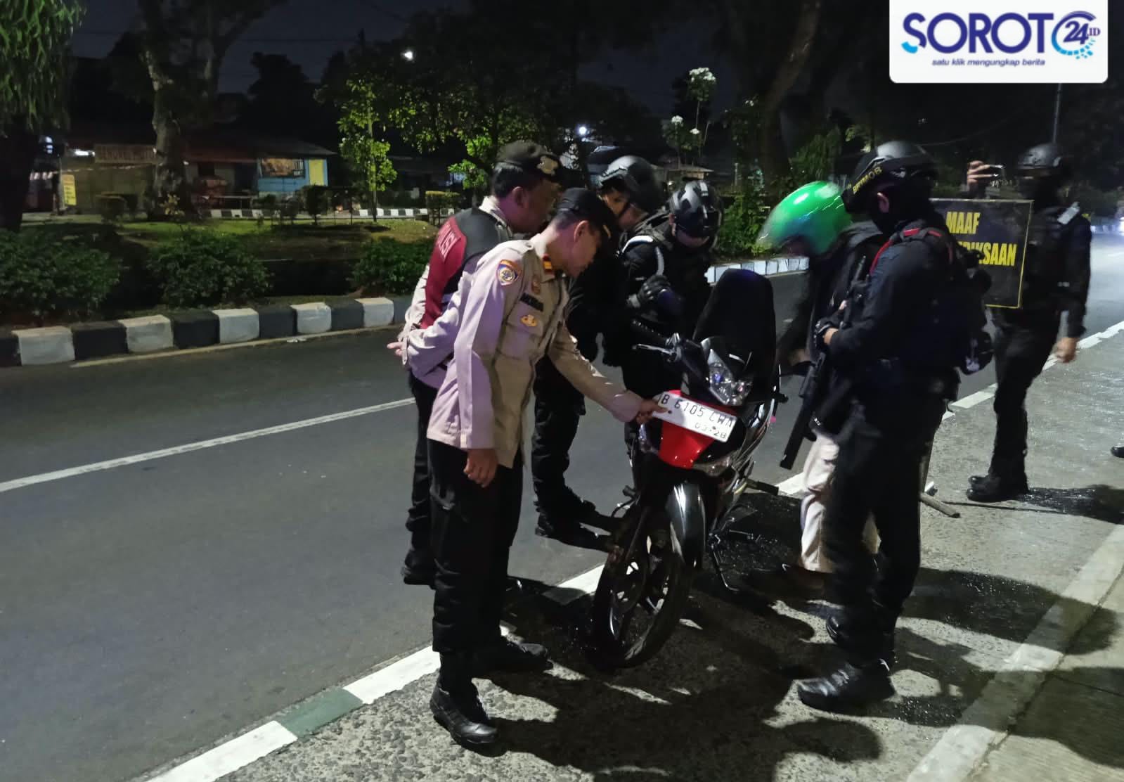 Beberapa petugas polisi memeriksa bagian depan motor matic merah di pinggir jalan saat malam hari