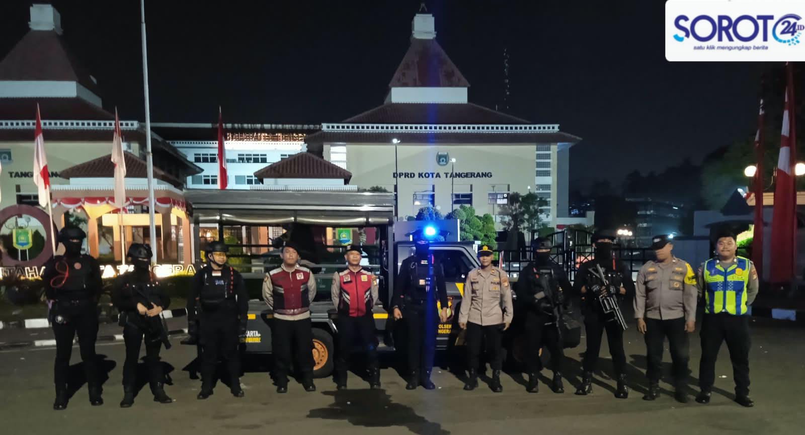 Sekelompok polisi berseragam coklat dan hitam lengkap dengan senjata laras panjang berdiri berbaris di depan gedung DPRD Kota Tangerang malam hari